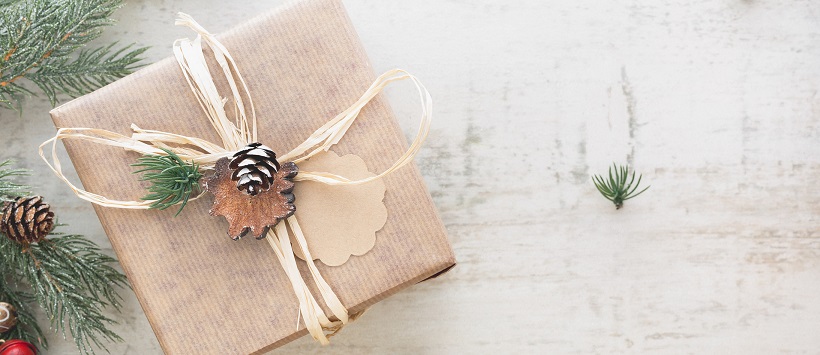 Brown paper package with straw ribbon and a pinecone ornament surrounded by Christmas tree needles.