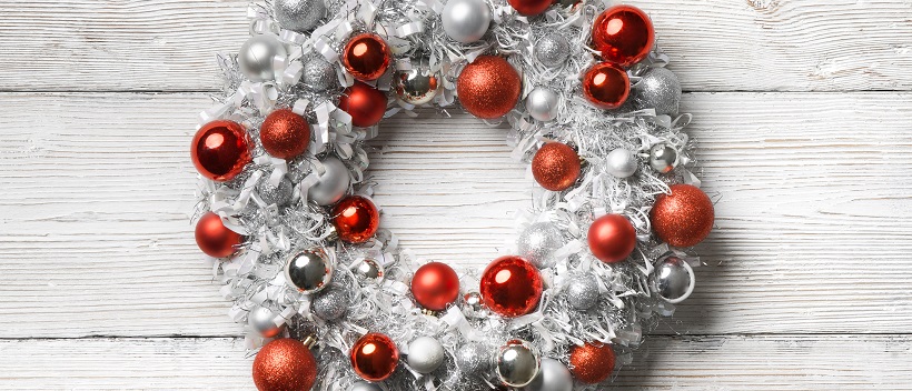 White wreath adorned with red and silver ornaments and placed on a white wooden background.