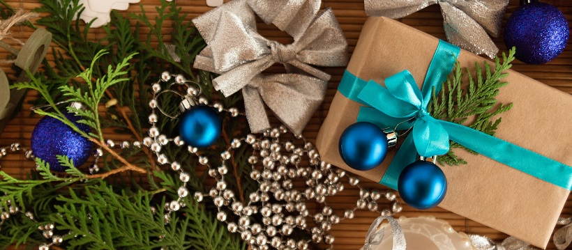 Christmas tree branches, silver beading, silver bows, and a brown package with a turquoise ribbon and blue ornaments.