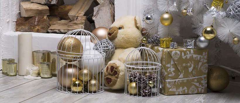 Under a white Christmas tree adorned with gold and silver ornaments, beige, white, and gold packages and decor sit with a wood pile in the background.