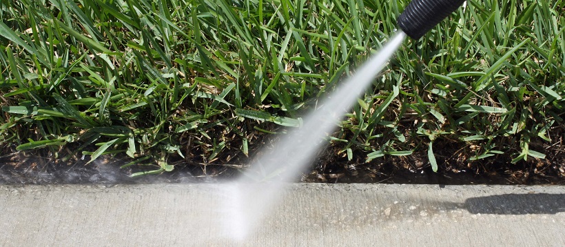 Close up of a patio near grass getting powerwashed.