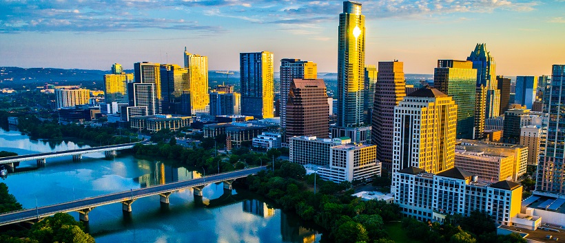 The sun casts a yellow hue over the skyrises in downtown Austin, Texas, and the fading blue sky is reflected in the clear, calm waters of Lady Bird Lake.