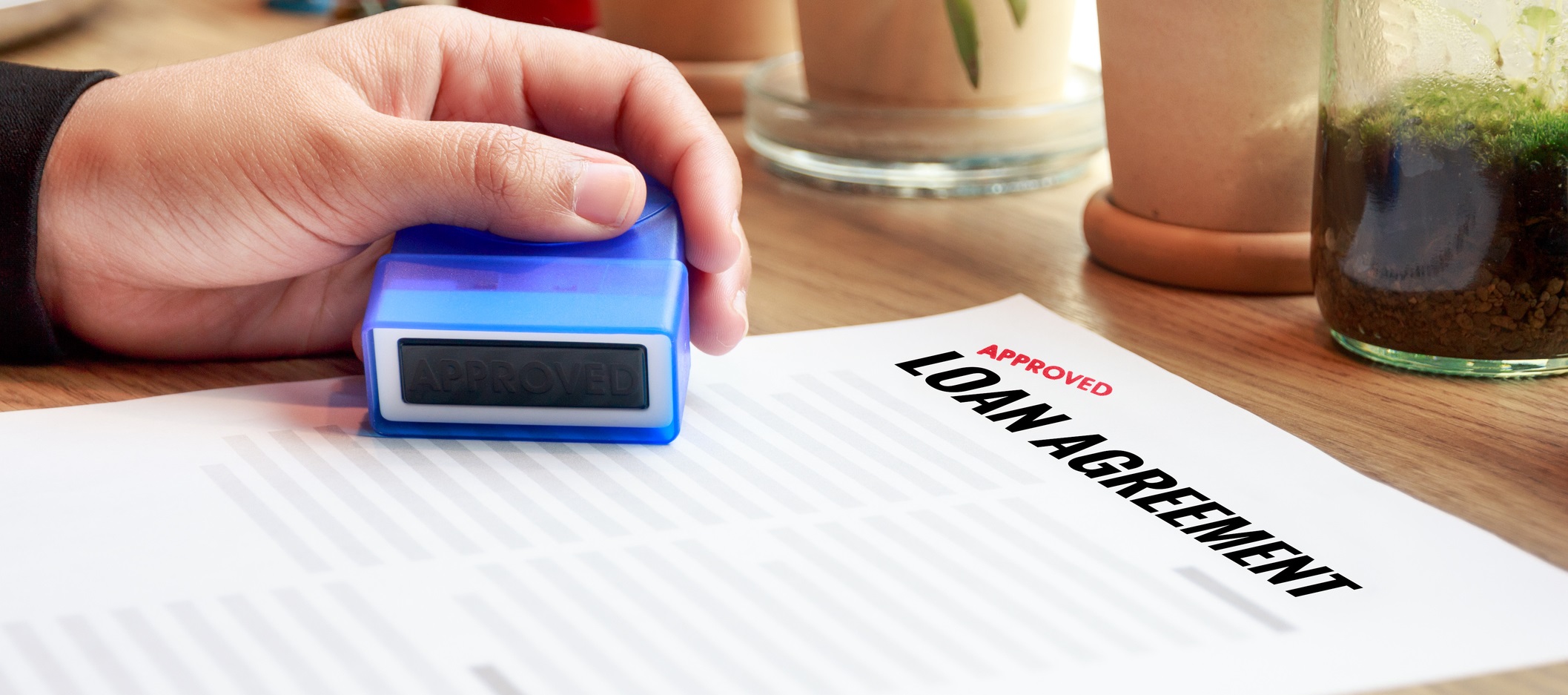 A person is holding a stamp over a piece of paper that reads ‘Approved loan agreement’.