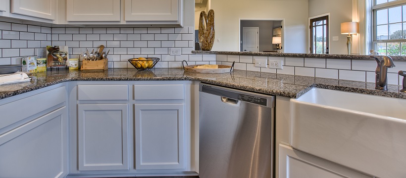 Kitchen with white cabinetry, granite, a stainless-steel dishwasher, and a deep farmhouse sink.