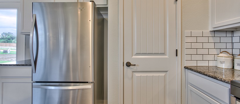 View of kitchen with stainless steel fridge next to a white pantry door.