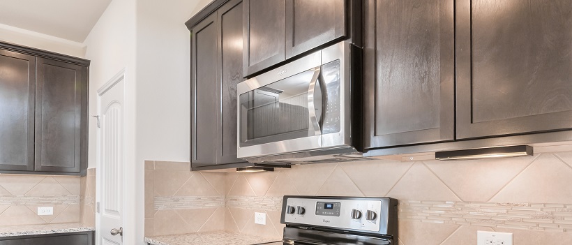 Kitchen view of a stainless steel microwave in between dark wooden cabinets and above a stove.