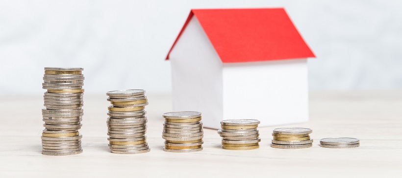 Stacks of coins decreasing in front of a miniature home with a red roof.