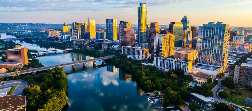 Sunset casts orange hues while creating blue shadows on the Austin cityscape with the Lady Bird Lake reflecting the sky above.