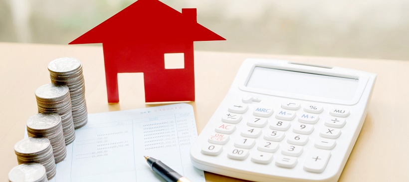 Stacks of coins, paper, pen, calculator, and paper cut-out of a house depicts financial aspect of buying homes in Austin, Texas.