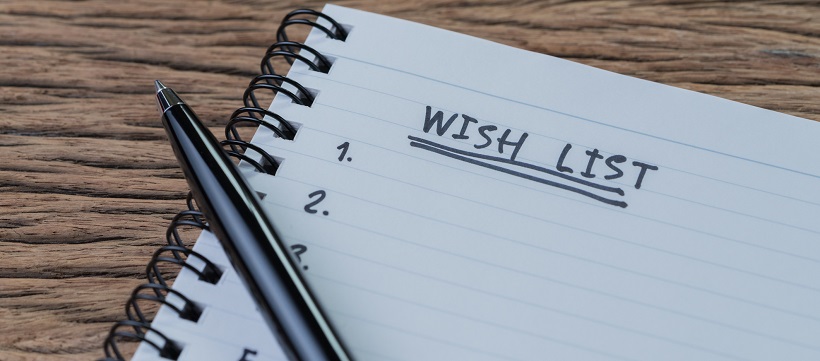 Notepad with the words “Wish List” and numbers with pen sitting on top of paper.